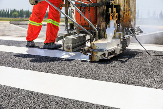 Road workers use hot-melt scribing machines to painting pedestrian crosswalk on asphalt road surface in the city.