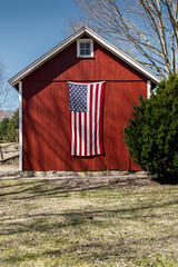 United States Flag hanging on an old New England red barn in the spring time © Bruce Peter Morin