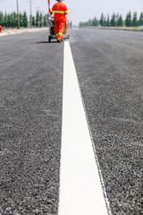 Road workers use hot-melt scribing machines to painting dividing line on asphalt road surface in...
