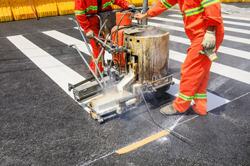 Road workers use hot-melt scribing machines to painting pedestrian crosswalk on asphalt road surface in the city. - obrazy, fototapety, plakaty