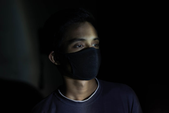 Young sick boy wears a black safety mask over dark background.Mask prevents  corona virus and air pollution dust.Portrait of young boy wearing a mask  and crying.Corona virus mask protection concept N Stock