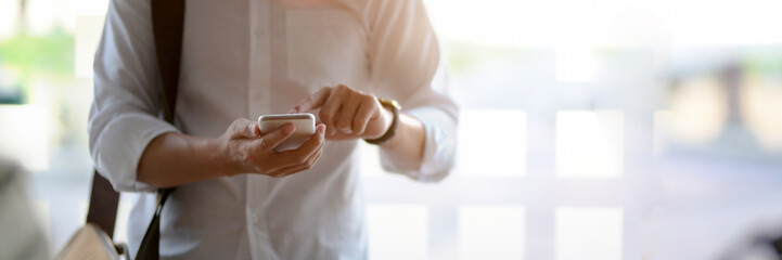 Cropped shot of male entrepreneur using smartphone in glass wall office