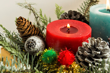 A burning red candle, designed in wooden basket with pine cones and leaves