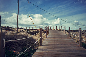 Algarve Faro coastline view. Wooden pathway, blue cloudy sky