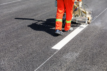 Road workers use hot-melt scribing machines to painting dividing line on asphalt road surface in...