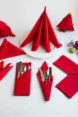 In different shapes folded,red color  paper napkins on the white with cutlery set and plate.Preparation for Christmas or New Year Feast.General view of napkins with vertical image