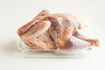 Frozen,cleaned and uncooked turkey in the glass oven container on the white surface.