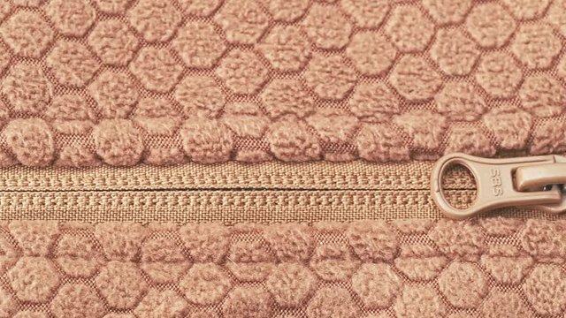 Brown ornamented fabric with zipper, close shot. Dolly shot of knitted fabric with abstract pattern and zipper. Brown diaper texture, abstract background