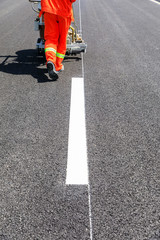 Road workers use hot-melt scribing machines to painting dividing line on asphalt road surface in...