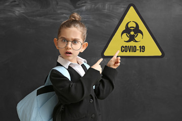 Scared little schoolgirl with warning sign on dark background. Concept of Coronavirus epidemic