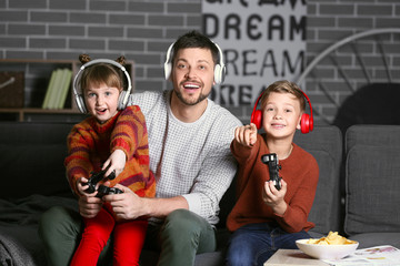 Father and his little children playing video games at home in evening