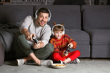 Father and his little daughter playing video games at home in evening