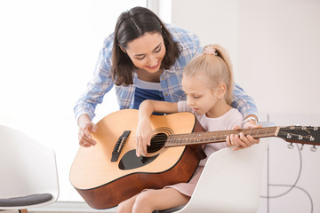 Private music teacher giving guitar lessons to little girl at home