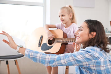 Private music teacher giving guitar lessons to little girl at home