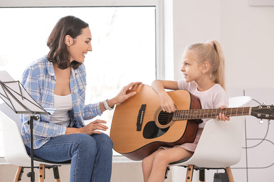 Private music teacher giving guitar lessons to little girl at home