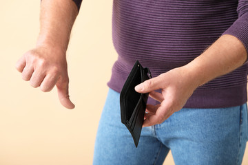 Senior man with empty purse showing thumb-down on color background, closeup