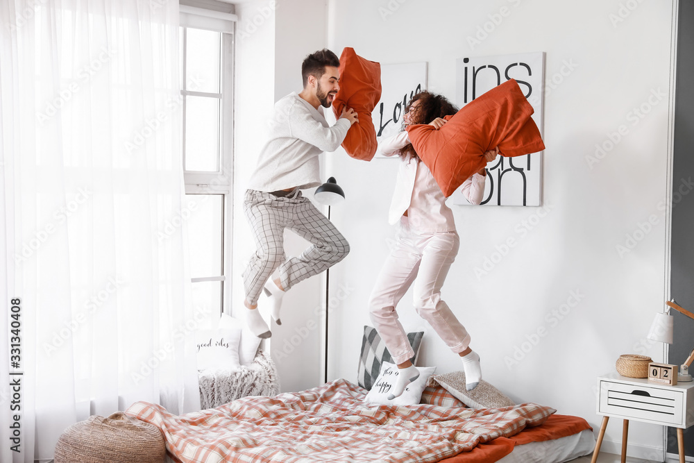 Poster Happy young couple fighting on pillows in bedroom