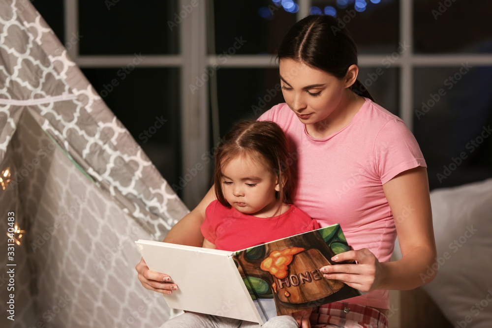 Wall mural Mother and her little daughter reading bedtime story at home