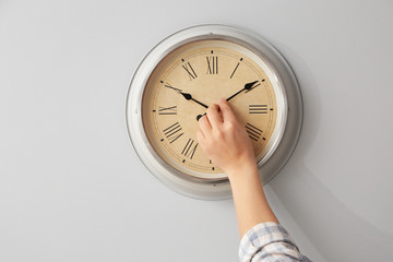 Young man touching arrows of clock on light wall