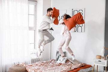 Happy young couple fighting on pillows in bedroom