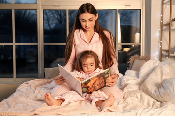 Obraz premium Mother and her little daughter reading bedtime story at home