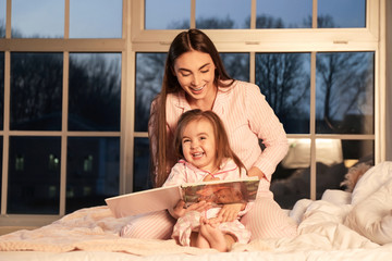 Mother and her little daughter reading bedtime story at home