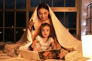 Mother and her little daughter reading bedtime story at home