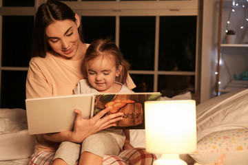 Mother and her little daughter reading bedtime story at home