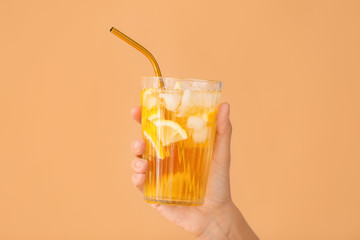 Female hand with cold tea in glass on color background