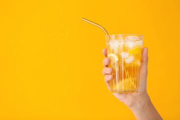 Female hand with cold tea in glass on color background