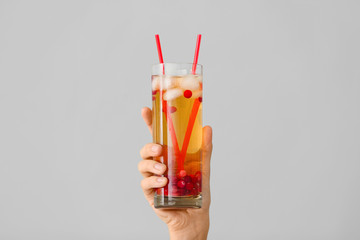 Female hand with cold tea in glass on grey background