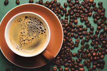 Cup of hot coffee and beans on color background