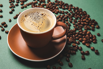 Cup of hot coffee and beans on color background