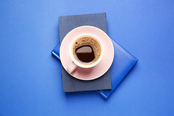 Cup of hot coffee and books on color background