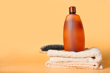 Shampoo, brush and towel on color background