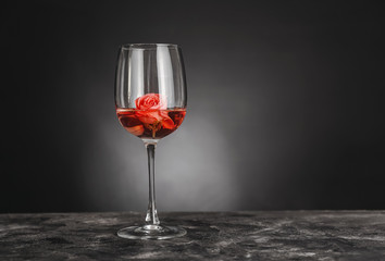 Glass of wine and rose on table against dark background