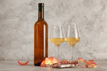 Bottle of wine, glasses, rose petals and candles on table