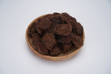 The dried plum is in a wooden bowl. It's on a white background