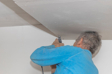 Worker is using screwdrivers to attach plasterboard to the ceiling.