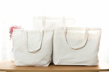 White canvas bags of various sizes, bathed in the sunshine at the window on the wooden table, are simple and fashionable