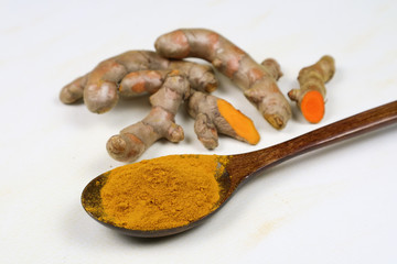 Turmeric powder in a wooden spoon and fresh turmeric roots isolated on a white background is an ingredient in turmeric foods and ingredients in skin care products. Turmeric helps the skin to be strong