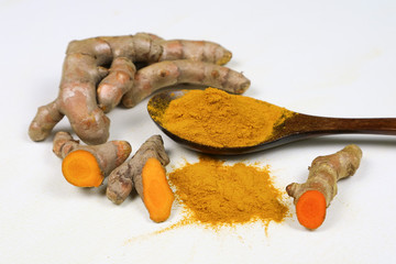 Turmeric powder in a wooden spoon and fresh turmeric roots isolated on a white background is an ingredient in turmeric foods and ingredients in skin care products. Turmeric helps the skin to be strong