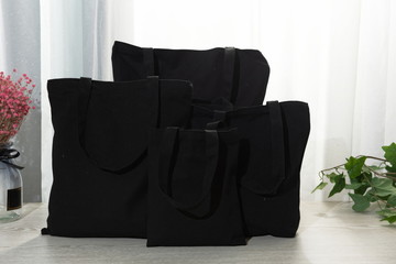 Black canvas bags of various sizes, bathed in the sunshine at the window on the wooden table, are simple and fashionable