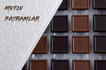Bitter and milky chocolate madlen in own box and writting on Happy Feast greeting words in Turkish with chocolate paint font.