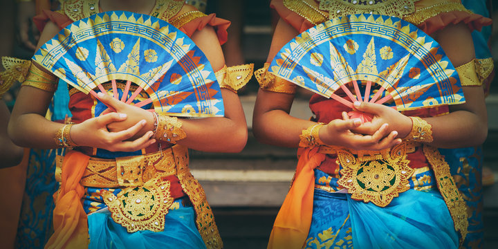 Asian travel background. Group of beautiful Balinese dancer women in traditional Sarong costumes with fans in hands dancing Legong dance. Arts, culture of Indonesian people, Bali island festivals.