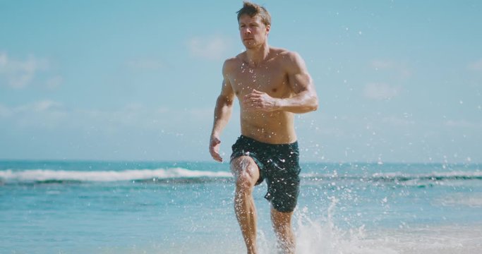 Young attractive muscular man running on the beach in slow motion, baywatch body, beach workout run