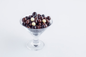 Elegant dark ball chocolates in glass candy bowl at white with copy space.