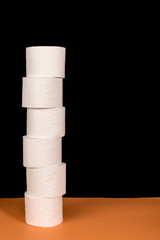 Rolls of toilet paper arranged on orange surface and black background with space for text.  Ideal for tissue paper shortage signs