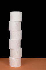 Rolls of toilet paper arranged on orange surface and black background with space for text.  Ideal for tissue paper shortage signs
