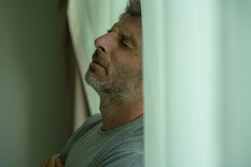 mid adult man crying sad and depressed standing at bedroom window in despair at home feeling worried and overwhelmed suffering depression and anxiety problem